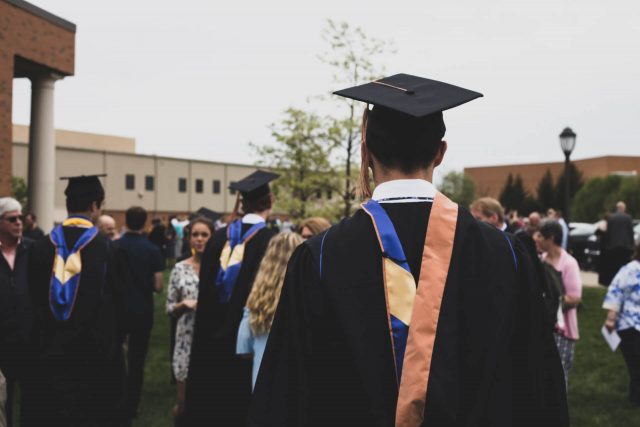 Imagem de um graduado de costas para a câmera, mas de frente para um grupo de graduados a comemorar.